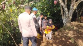 Kapolsek Putri Betung, Ipda Novrizal SH bersama personel membantu mengevakuasi seorang warga yang sedang menggendong bayi saat melintasi lokasi longsor susulan di Putri Betung, Senin (5/1/2026).