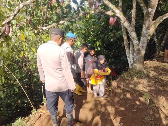 Kapolsek Putri Betung, Ipda Novrizal SH bersama personel membantu mengevakuasi seorang warga yang sedang menggendong bayi saat melintasi lokasi longsor susulan di Putri Betung, Senin (5/1/2026).